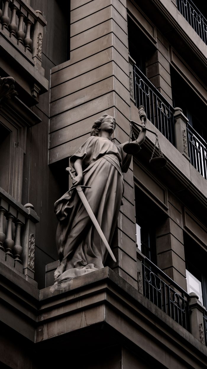 services-04 A sculpture of Lady Justice with a sword and scales on a city building's facade.